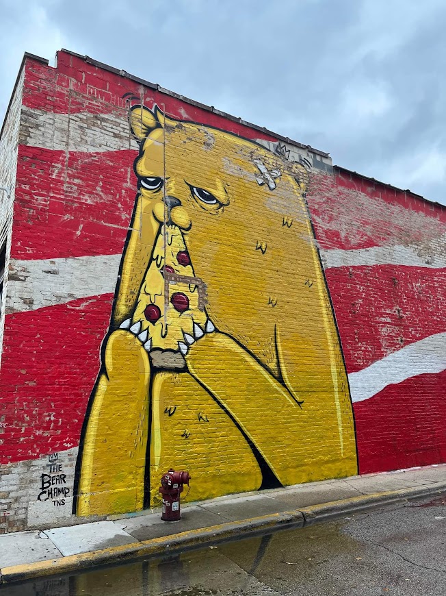 street art of yellow bear eating pizza